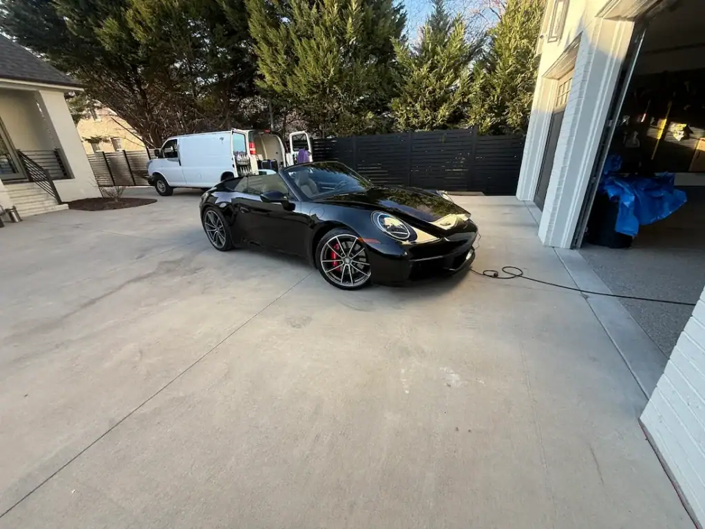 Black Porsche 911 Cabriolet after a mobile detail in a driveway, with the FC Auto Detailing van behind it